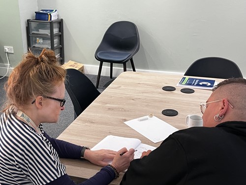 A learner and a tutor working together on paperwork at a table