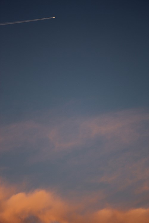 An aeroplane vapour trail across a dusk sky above pink clouds