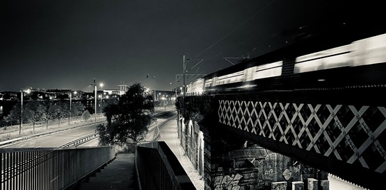 A train crossing a lattice railway bridge at night, in black and white
