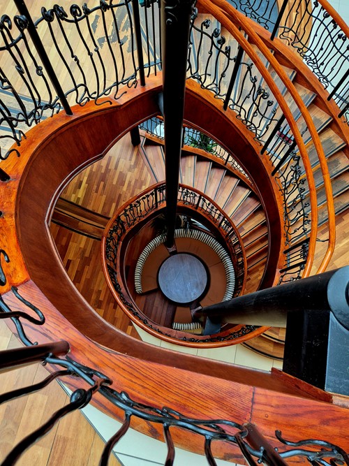 Looking down a wooden spiral staircase with ornate ironwork railings