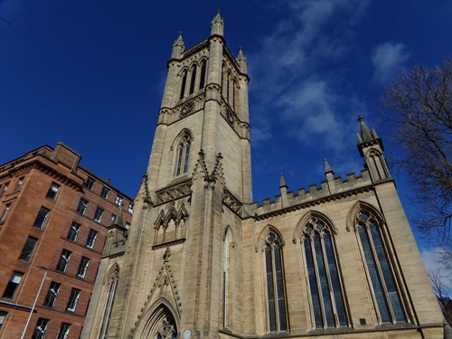 A sandstone church tower and tenement against a bright blue sky