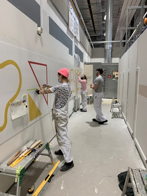 Students marking out a geometric mural along a warehouse corridor