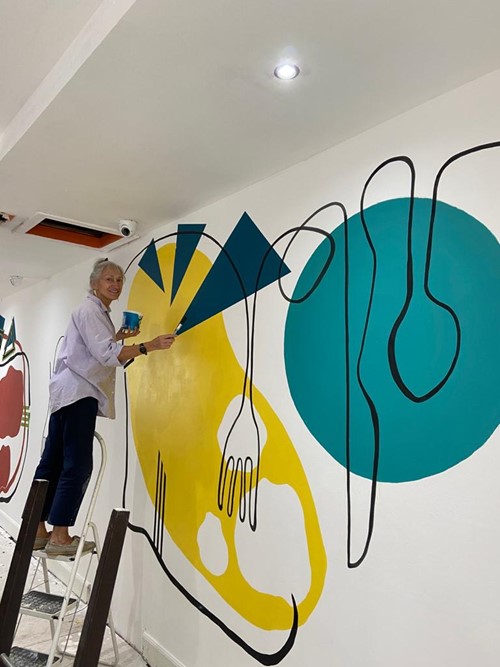 Artist on a step ladder painting a yellow and teal cutlery mural