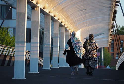 Two women walking together under the canopy of a footbridge at golden hour