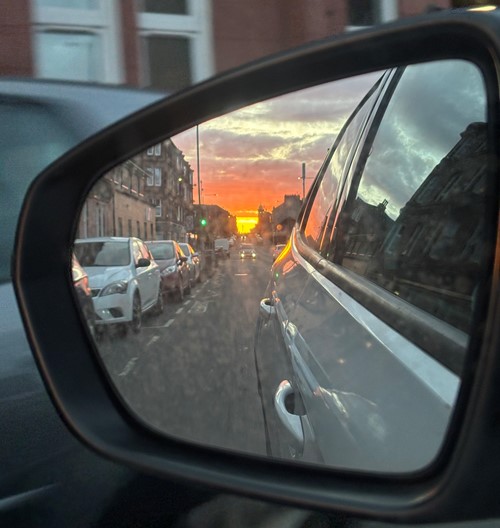 A fiery sunset down a tenement street seen in a car wing mirror