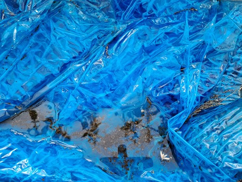 Creased blue tarpaulin sheeting with pooled water and debris