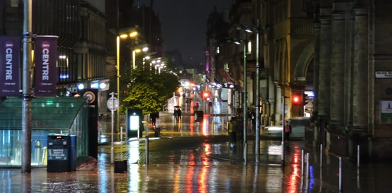 A rain-soaked Glasgow street at night with reflected neon lights