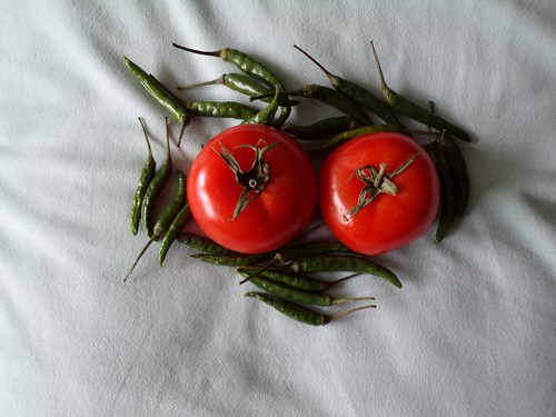 Two tomatoes surrounded by green chillies on a white cloth