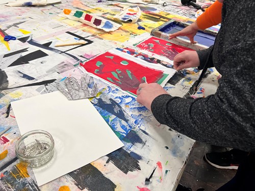 Learners screen printing colourful artwork on a paint-covered studio table